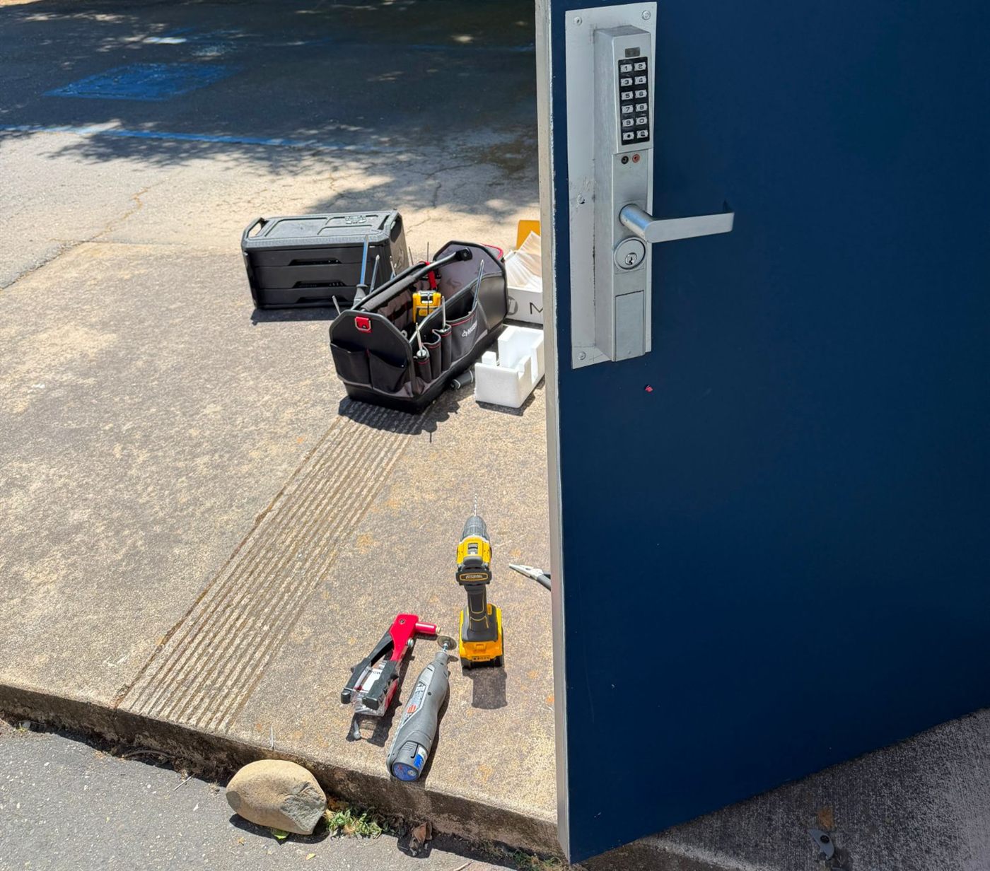 Keypad lever lock installed on a blue commercial steel door, with tools on the ground