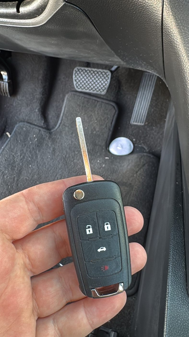 New flip key remote held inside a car near the pedals