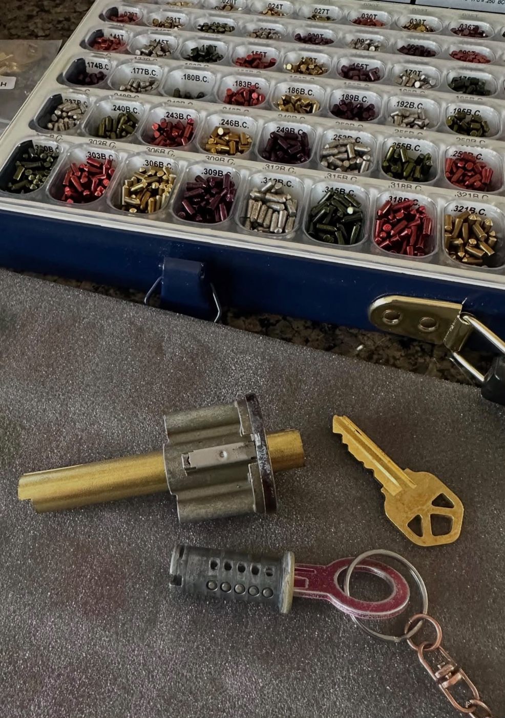 Lock cylinders and a new key next to an open tray of color-coded rekey pins