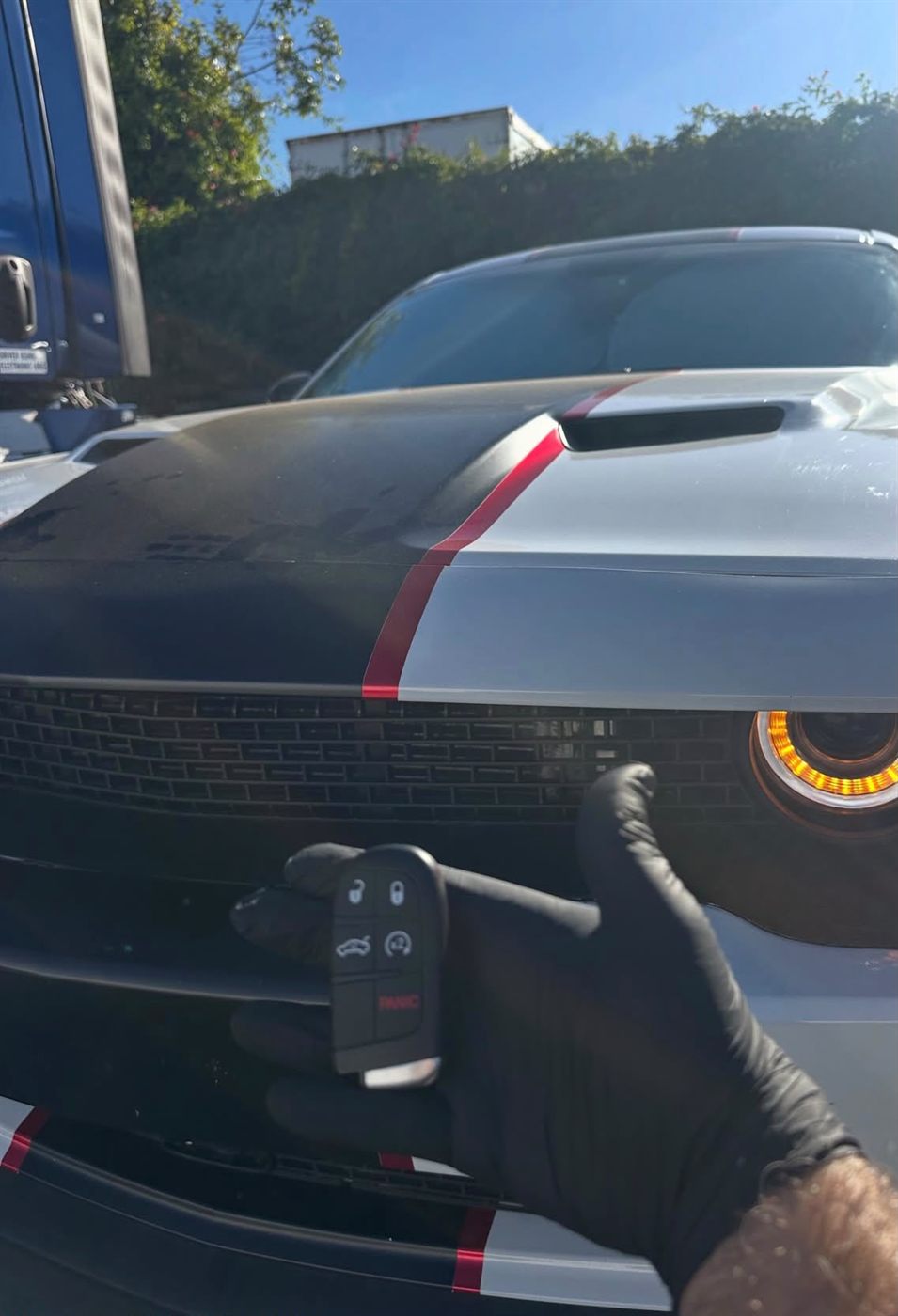 New five-button smart key held in front of a gray muscle car with racing stripes
