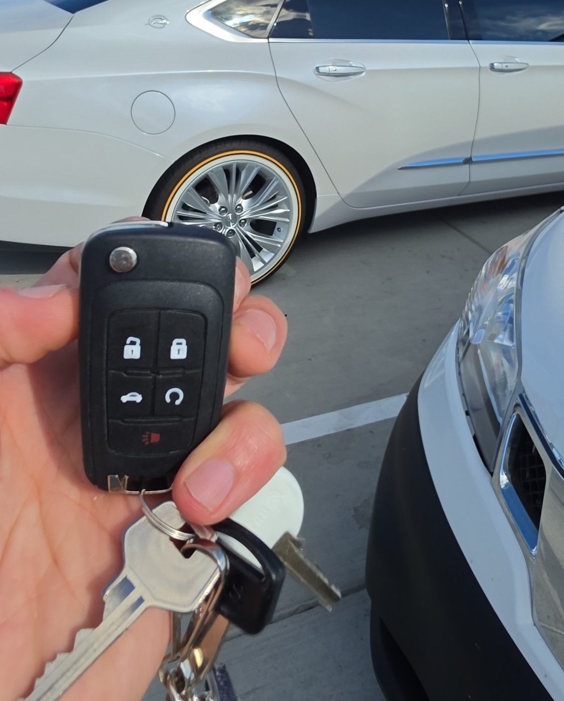New flip key remote held in front of a white sedan in a parking lot