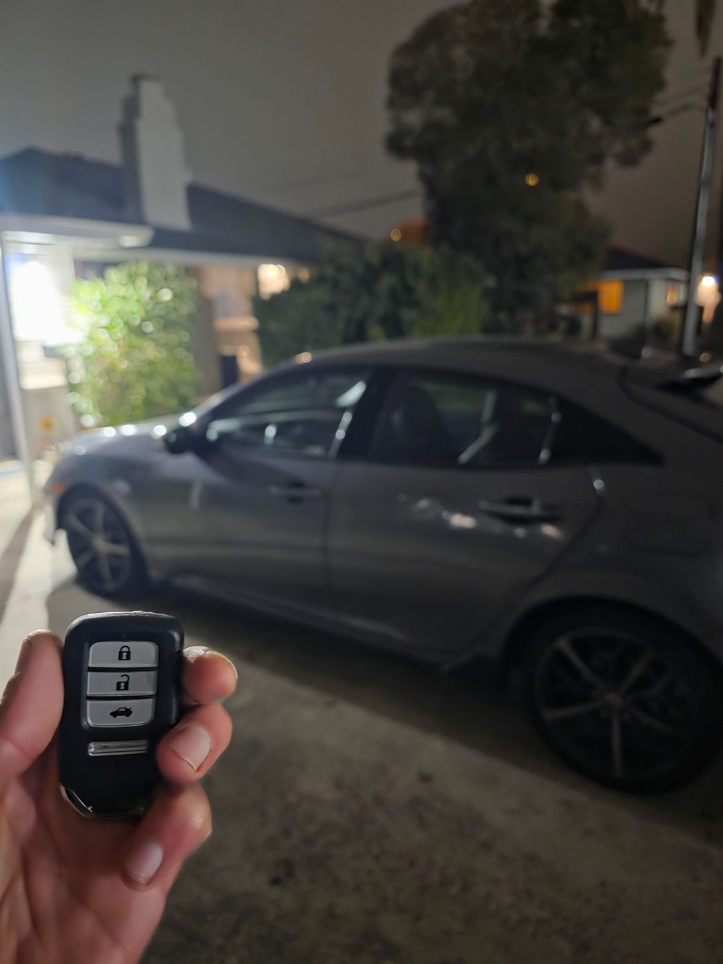 New smart key held up in front of a gray hatchback at night