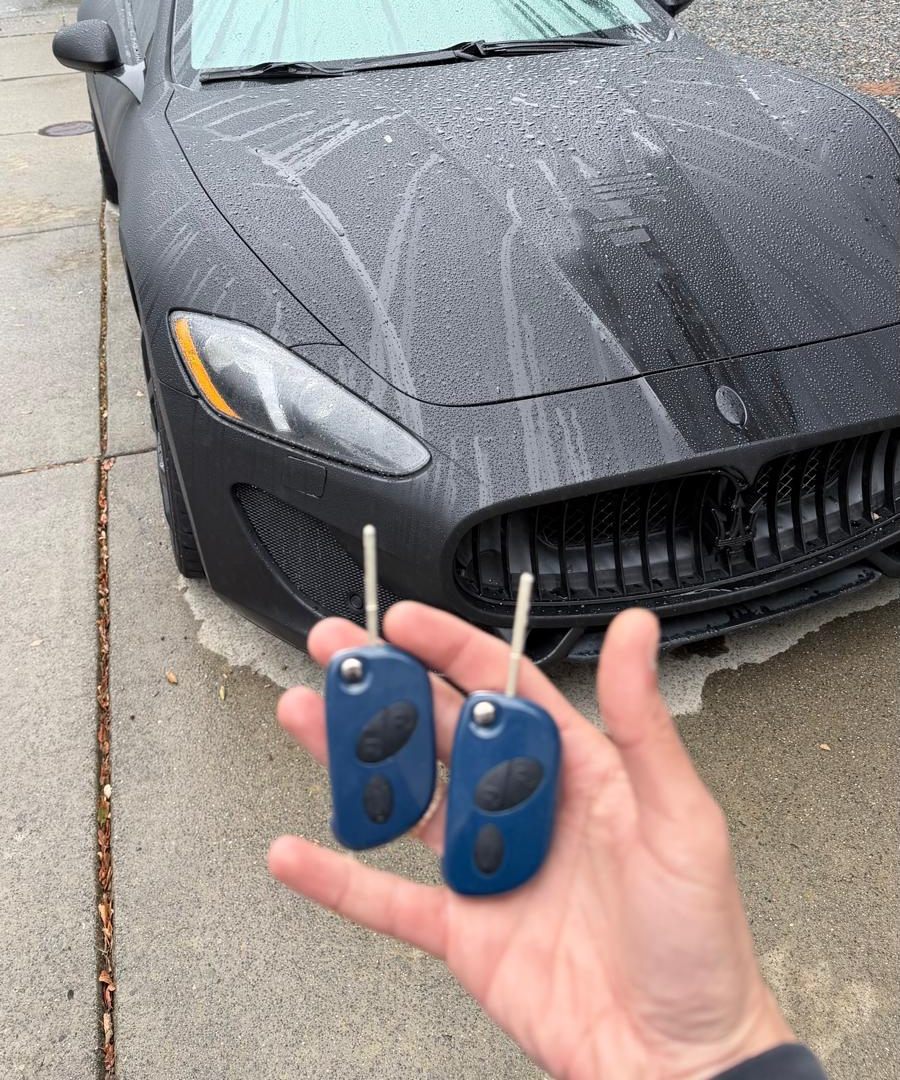 Two new blue flip keys held in front of a black sports car