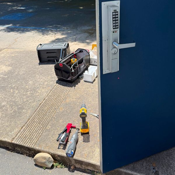 Keypad lever lock installed on a blue commercial steel door, with tools on the ground