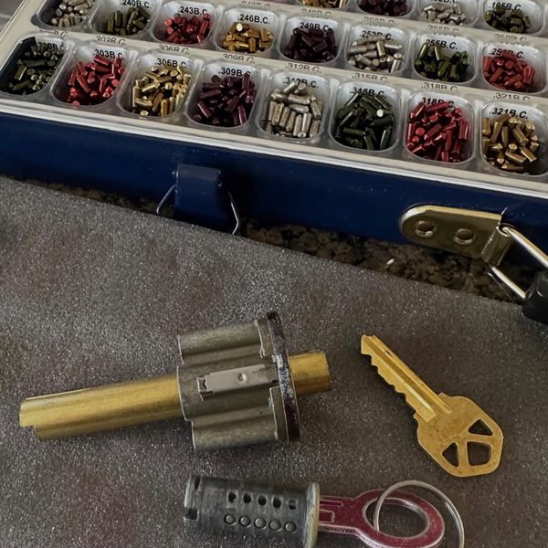 Lock cylinders and a new key next to an open tray of color-coded rekey pins