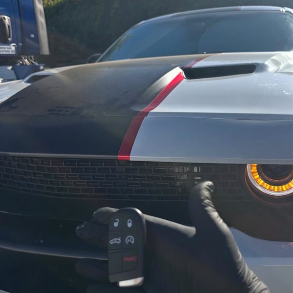 New five-button smart key held in front of a gray muscle car with racing stripes