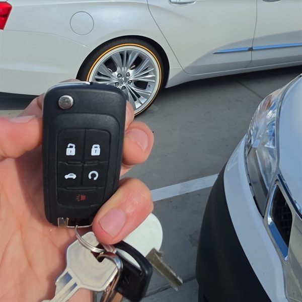 New flip key remote held in front of a white sedan in a parking lot