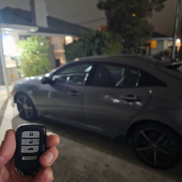 New smart key held up in front of a gray hatchback at night