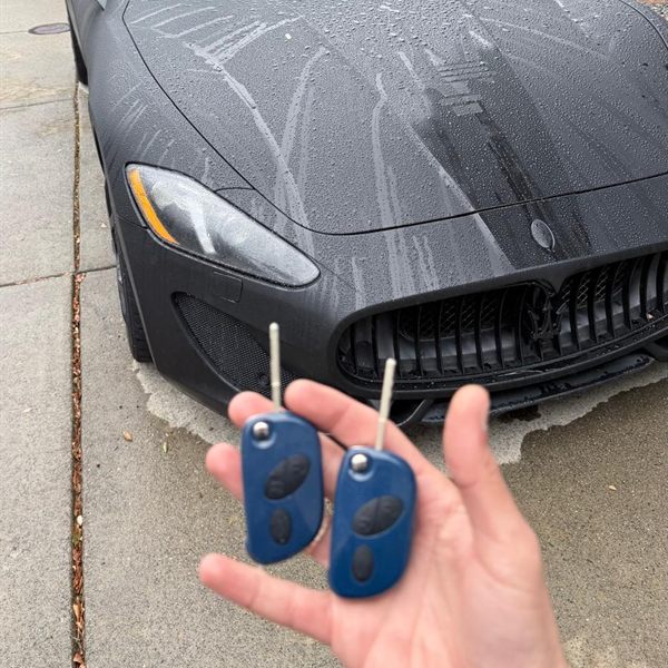 Two new blue flip keys held in front of a black sports car